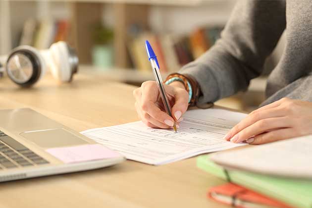 Pessoa escrevendo com uma caneta azul com um notebook na frente