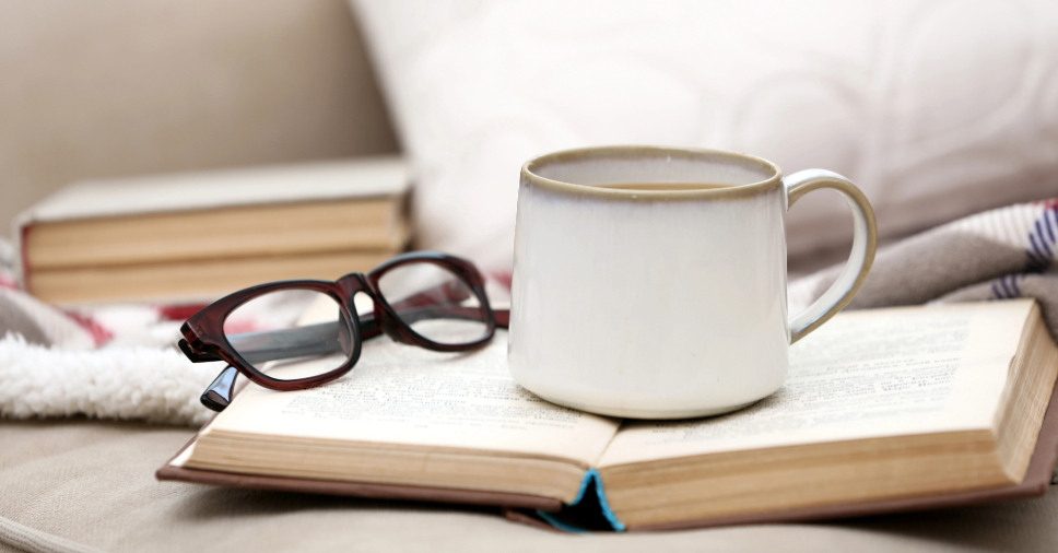 Livro aberto, óculos e caneca em cima de um sofá