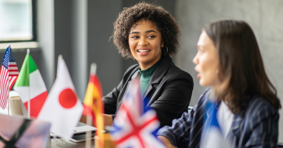 Mulheres conversando com bandeiras de países, representando o desenvolvimento profissional global.